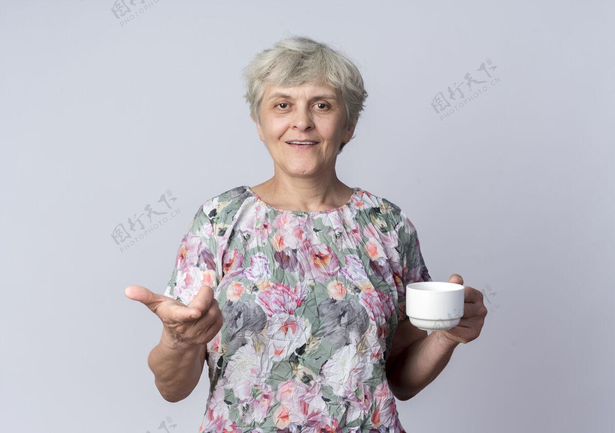 老人微笑着的老妇人手拿杯子 点着隔离在白墙上的东西微笑女人杯子
