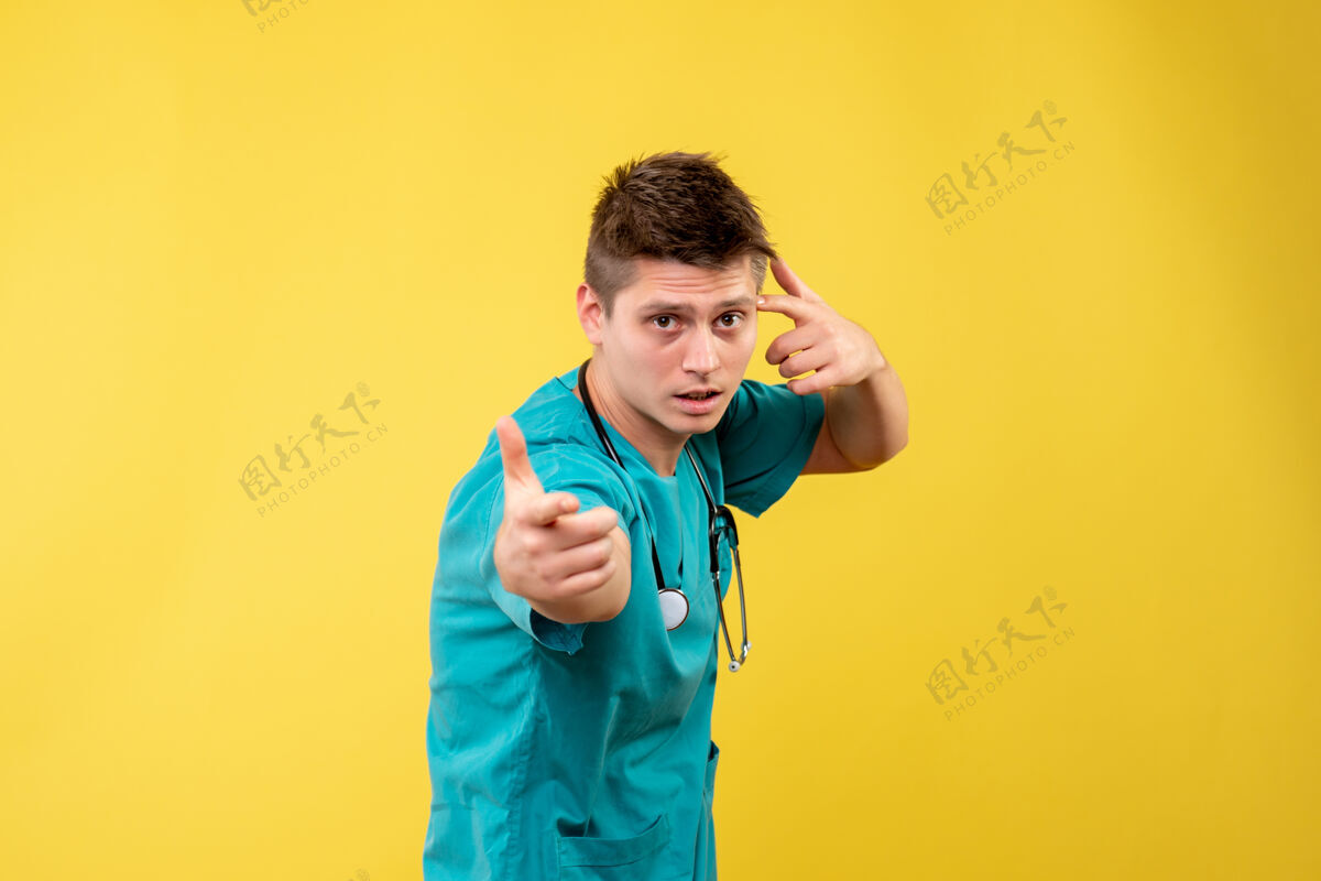 情绪黄色墙壁上穿着医疗服的男医生的正视图正面快乐套装
