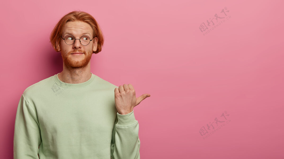 套头衫大胡子红头发的成年男子用拇指指向右侧促销拇指眼镜