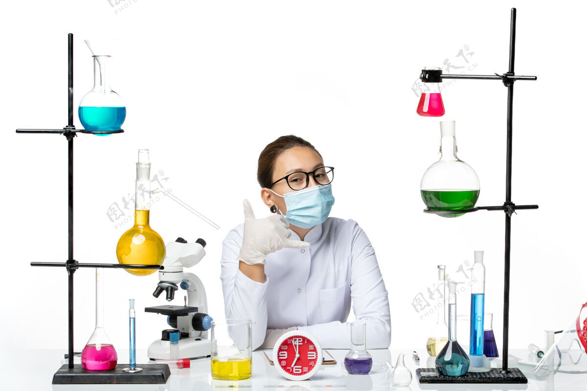 医学前视图穿着白色医疗服的女化学家带着面罩坐在白色背景上的溶液化学家实验室病毒-飞溅实验室前面西装