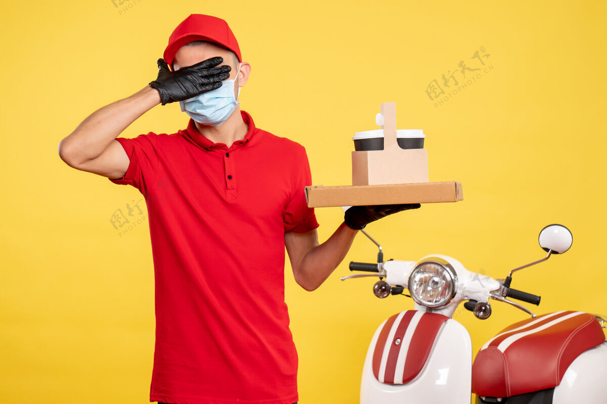送货正面图：戴着口罩的男快递员 带着递咖啡的盒子 眼睛蒙着黄色的服务盒 病毒工作服 大流行工作服黄色病毒面罩