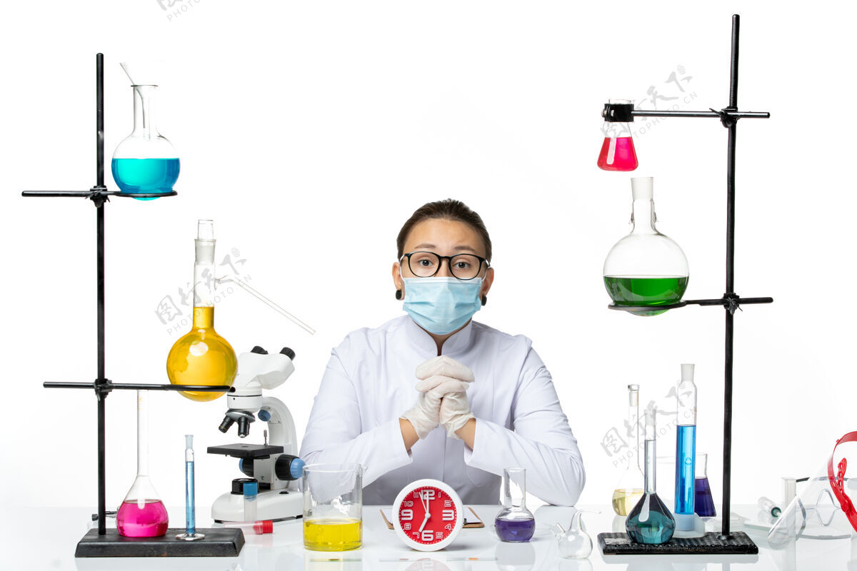 溶液正面图：身穿医疗服的女化学家戴着面罩坐在白色办公桌上 解决方案病毒实验室化学科维德飞溅科学喷溅实验室