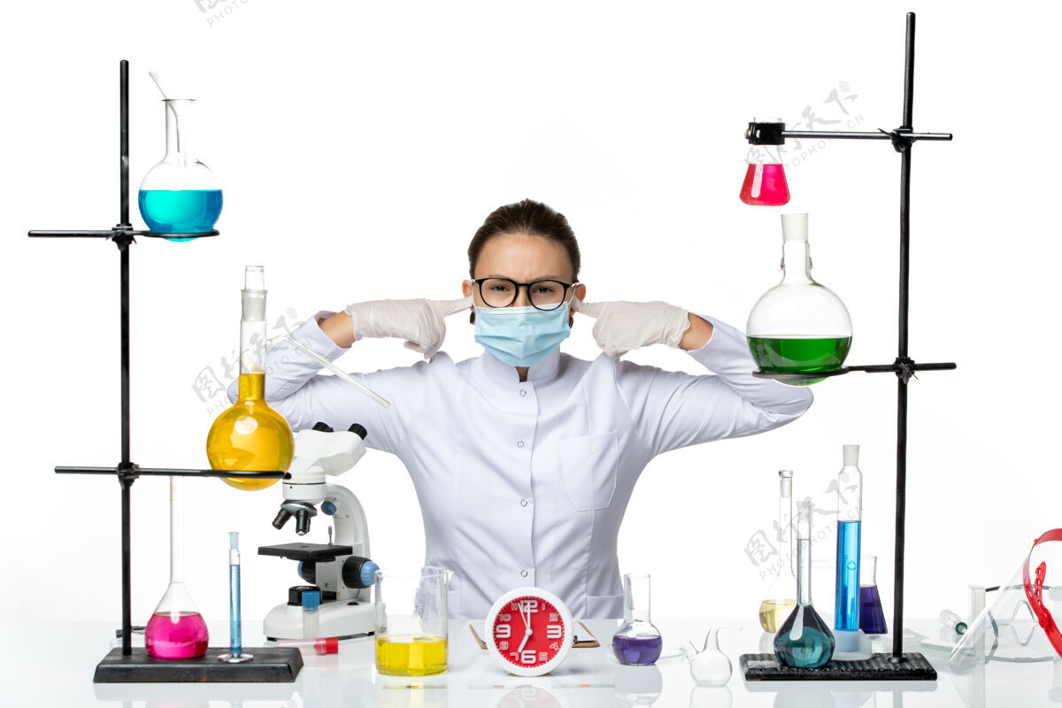 耳朵前视图穿着医疗服的女化学家 戴着面罩 坐在溶液里 在白色背景的化学病毒实验室里闭上耳朵-飞溅药物坐着化学