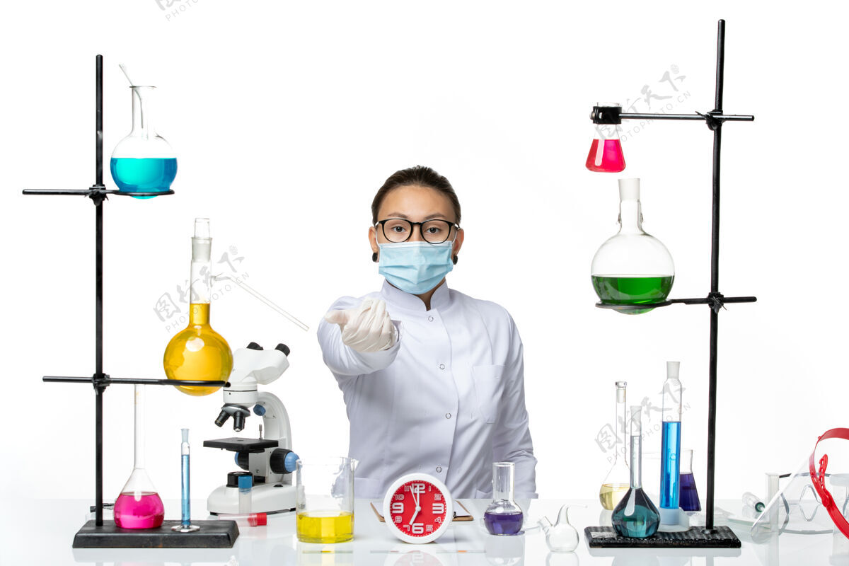 解决方案前视图穿着医疗服的女化学家戴着面罩 坐在白色背景上的化学实验室病毒-喷溅实验室坐西装