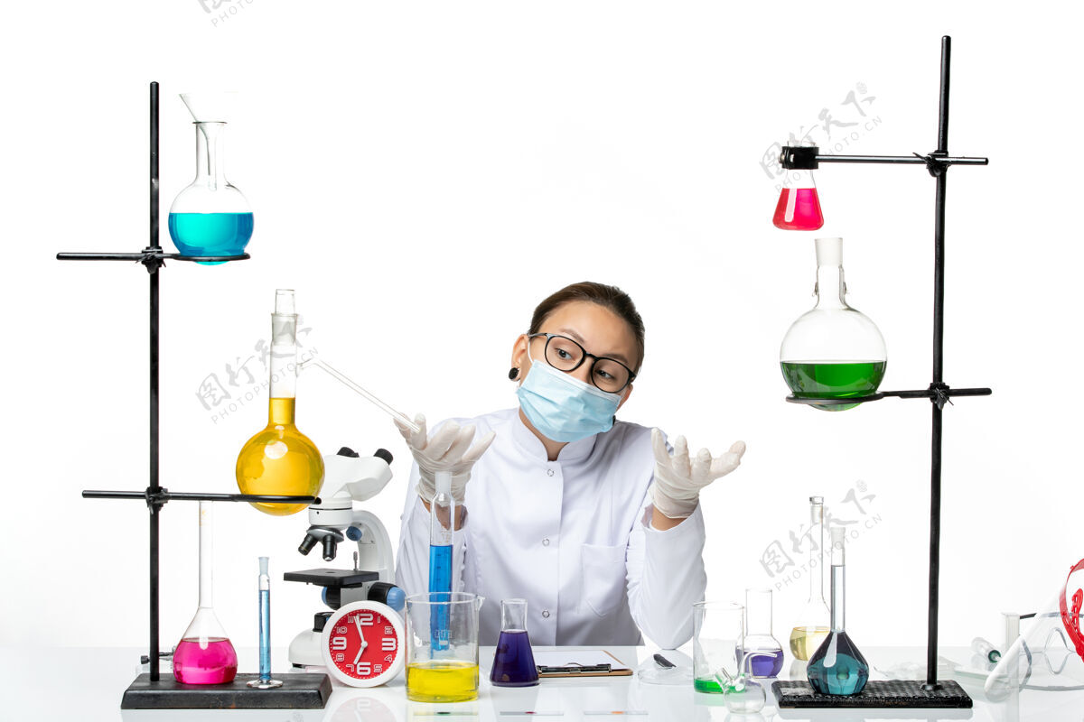 喷溅前视图穿着医疗服的女化学家戴着口罩坐在房间里 桌子上的溶液背景是白色的病毒化学实验室病毒飞溅房间实验室桌子