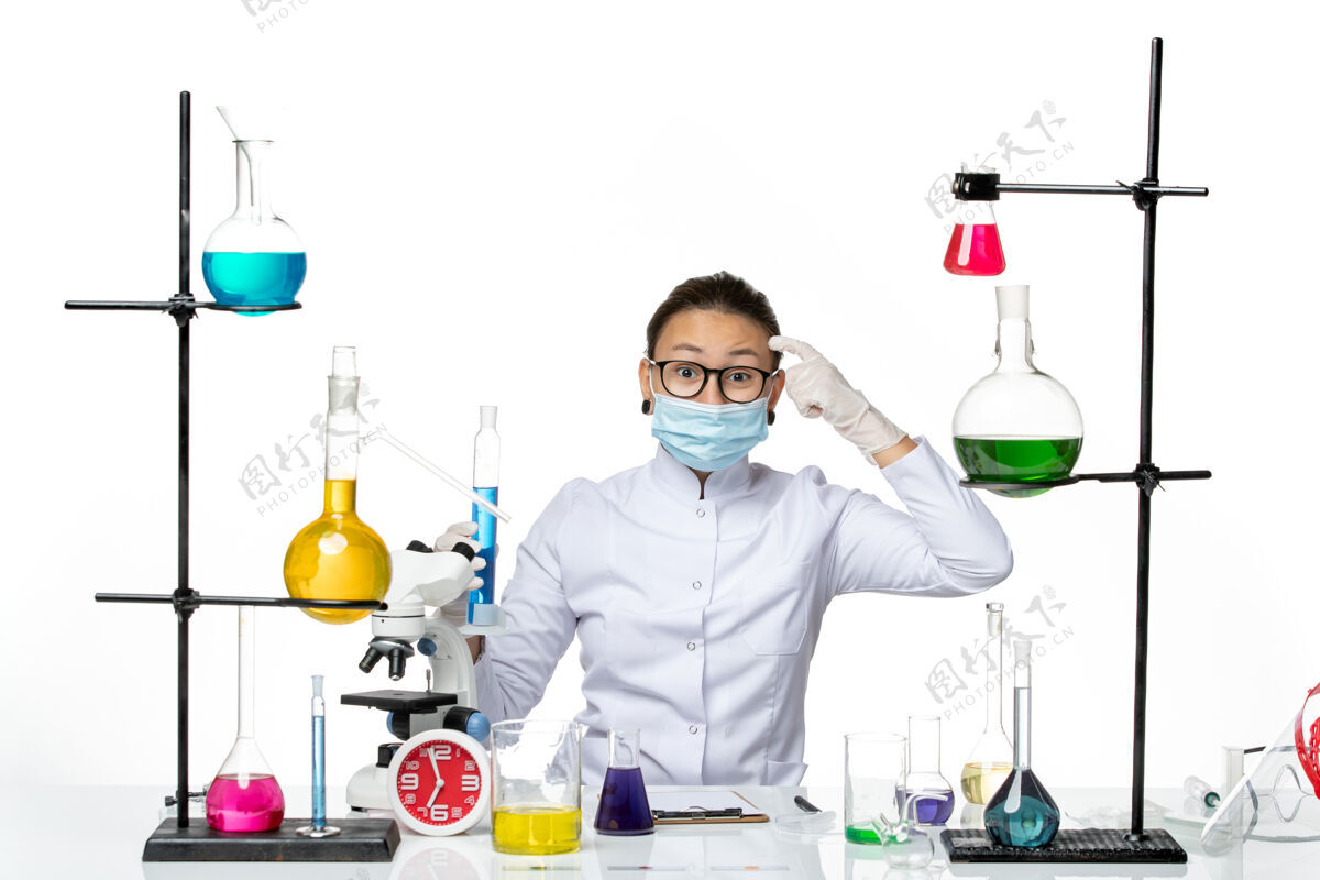 医生前视图：穿着医疗服的女化学家 戴着面罩 拿着白色背景上蓝色溶液的烧瓶 病毒化学实验室的covidsplash科学面罩实验室