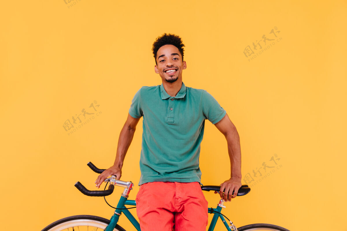 年轻快乐的黑人自行车手在笑英俊的非洲年轻人在他的自行车旁愉快地摆姿势时髦黄色室内