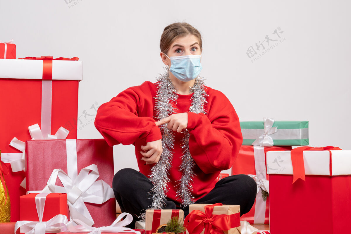 病毒正面图：年轻女性戴着无菌面具坐着 手里拿着圣诞礼物坐着礼物年份