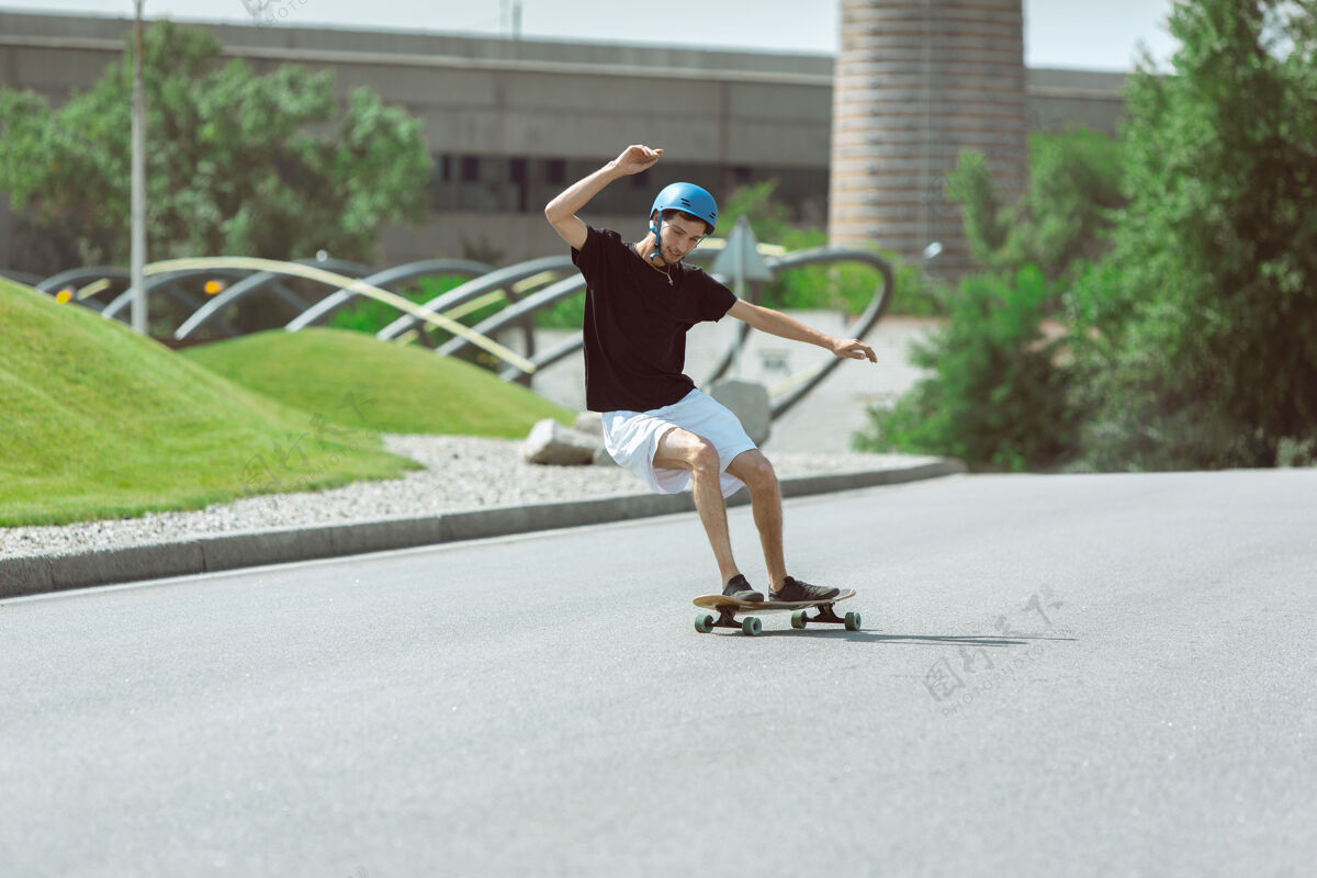 男性在阳光明媚的日子里 在城市街道上玩滑板的人穿着装备的年轻人在沥青路面上骑行和玩长板休闲活动 运动 极限 爱好和运动的概念实践技巧男孩