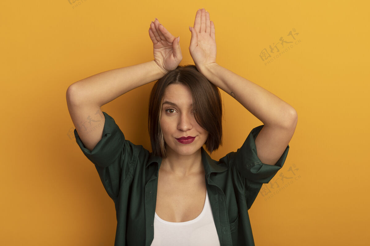 黑发自信漂亮的白种女人双手举过头顶 在橘子上做兔子耳朵的手势姿势成年人年轻