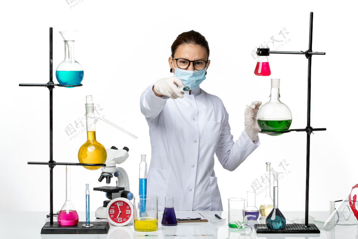 持有前视图：身穿医疗服的女化学家 戴着面罩 在白色背景上注射病毒化学实验室的covidsplash科学前面医生