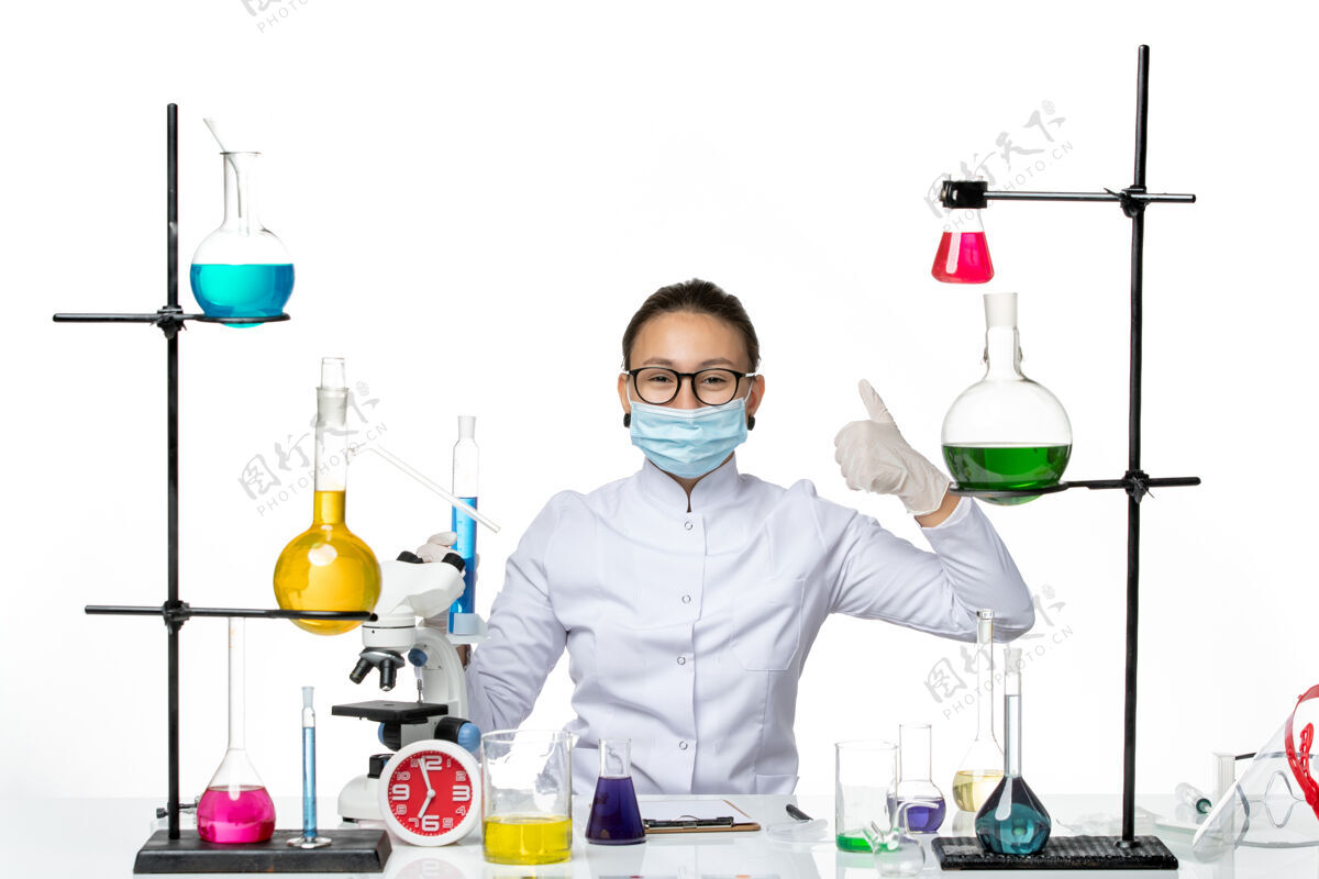 面具正面图：穿着医疗服的女化学家 戴着面具 拿着蓝色溶液的烧瓶 在白色背景上微笑 飞溅着病毒化学实验室的病毒喷溅医学医生