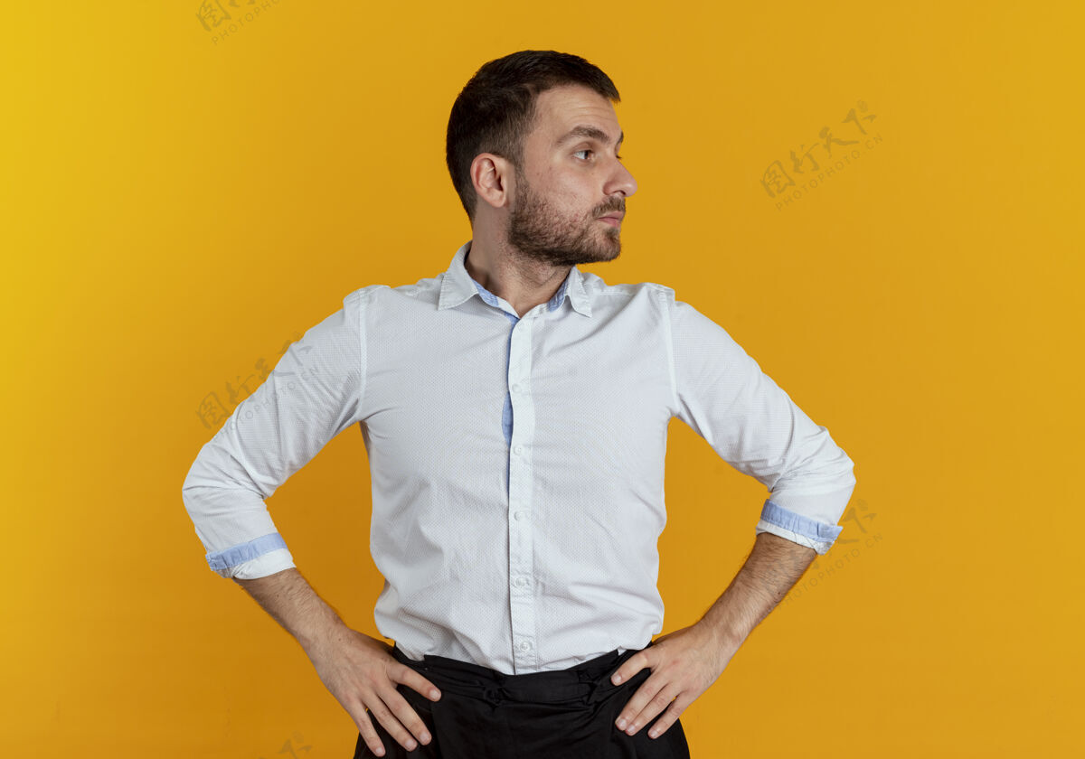 优雅自信的帅哥把手放在腰上看着橙色墙上孤立的一面侧身帅气自信