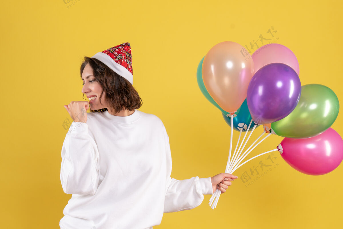 漂亮的女人正面图美丽的女性手持五颜六色的气球站在黄色多彩圣诞节举行