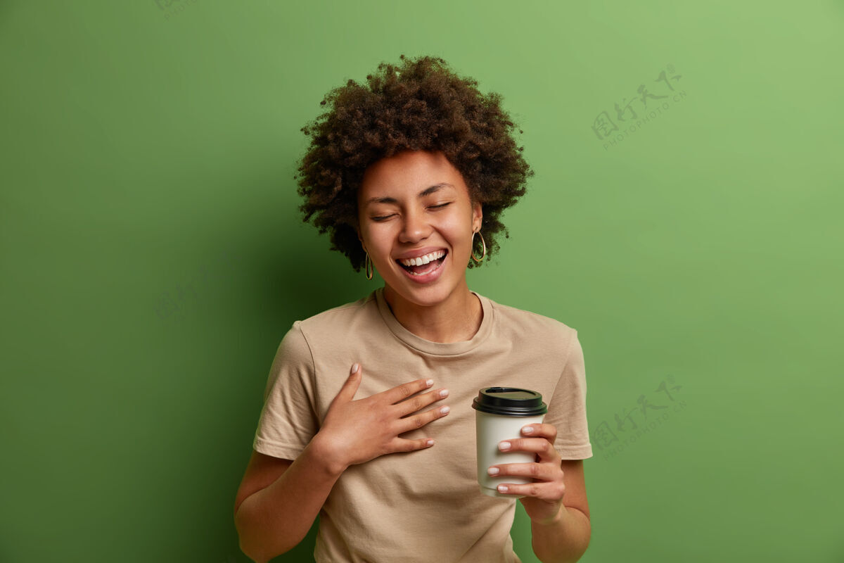 民族快乐的民族女孩的画像有乐趣和大声笑出来 举行一次性咖啡杯 微笑广泛和闭上眼睛 有愉快的交谈 隔离在绿色的墙壁生活方式的概念咖啡因牙齿卷曲的