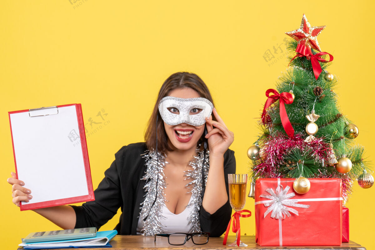 成人新年的心情与微笑迷人的女士穿着西服戴着口罩 手持文件在办公室黄色隔离持有面具时尚