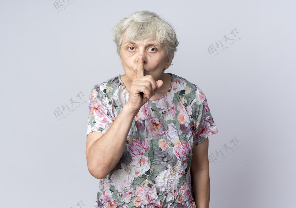 手势焦急的老妇人把手放在嘴上 示意安静的牌子孤立在白墙上女人安静手