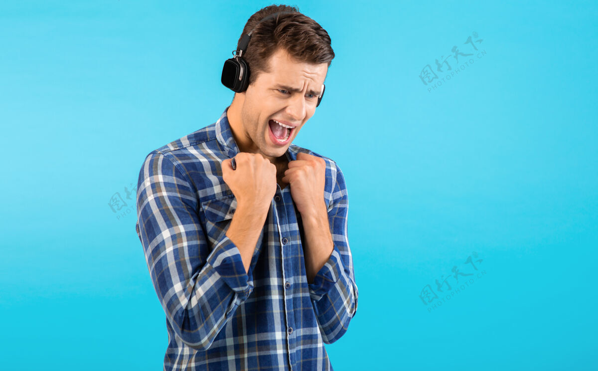 设备时尚帅气的年轻人 戴着无线耳机听音乐 玩得开心 现代风格 快乐的情绪 蓝色背景 穿着格子衬衫扬声器娱乐快乐