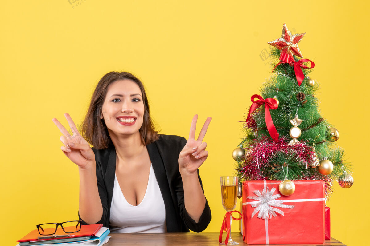 手势新年心情美丽的商务小姐用手指做着胜利的手势 坐在办公室的桌子旁坐手指人