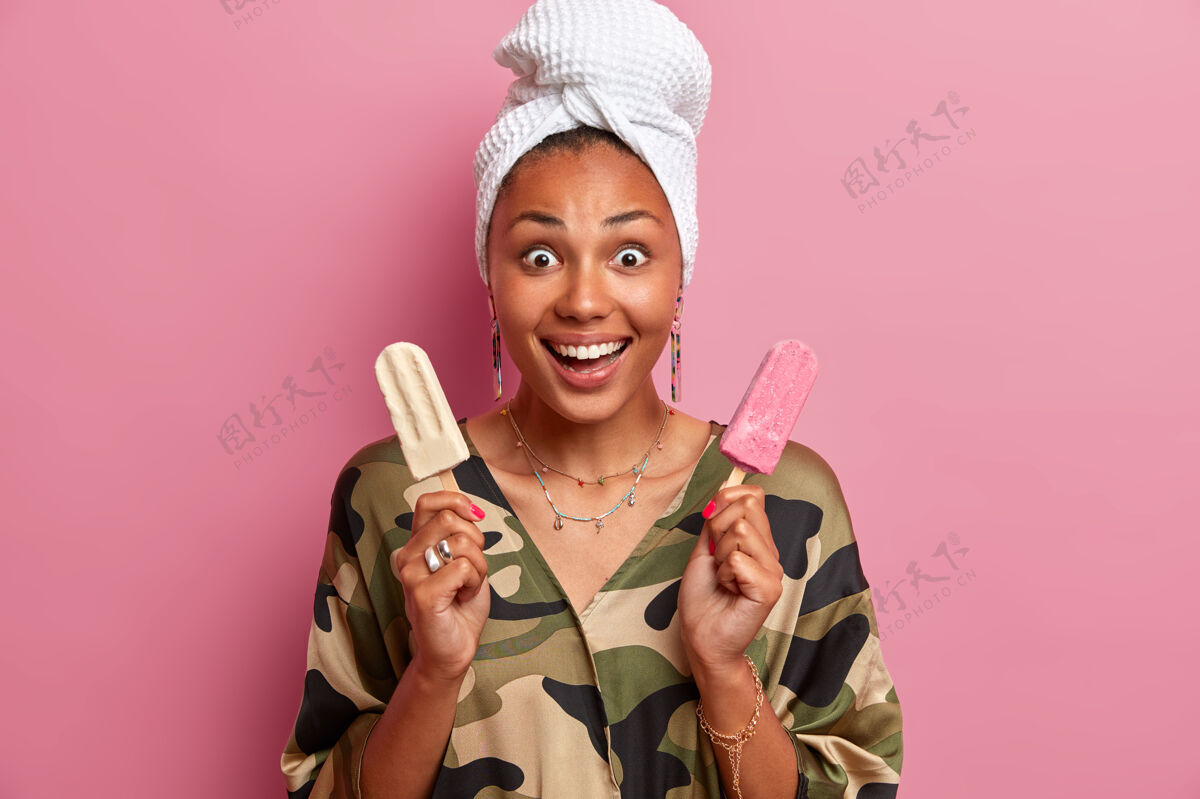 积极快乐的年轻非洲裔美国妇女在家里吃着美味的冰淇淋 穿着家常服 用冷冷冻甜点满足她的甜食 隔离在粉红色的墙上年轻请享受