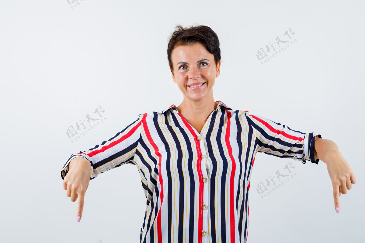 目录成熟的女人穿着条纹衬衫用食指指着下面 看起来很开心 正面视图女性老年女性