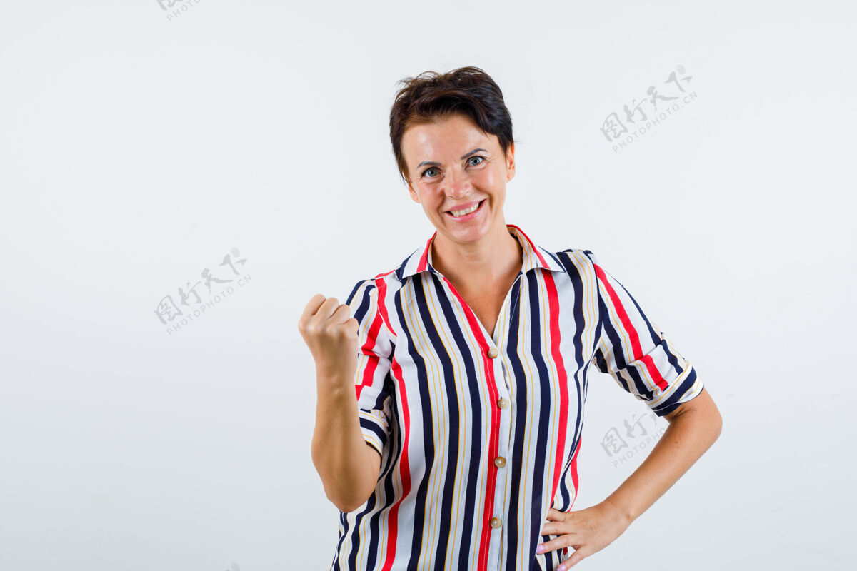 拳头成熟的女人握紧拳头 手放在条纹衬衫的腰上 看起来很自信正面图年龄前面成熟