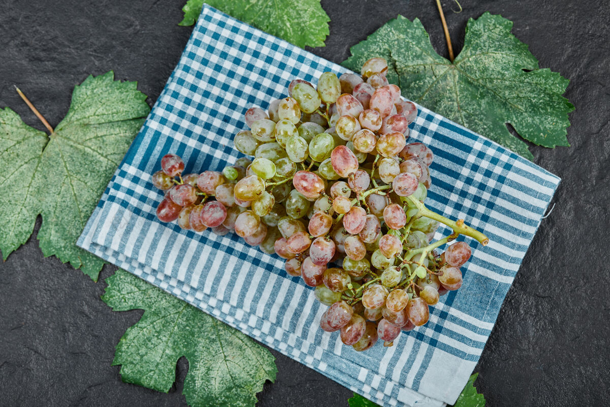 食物一簇带叶子的红葡萄和深色背景上的蓝色桌布高质量的照片季节新鲜叶子