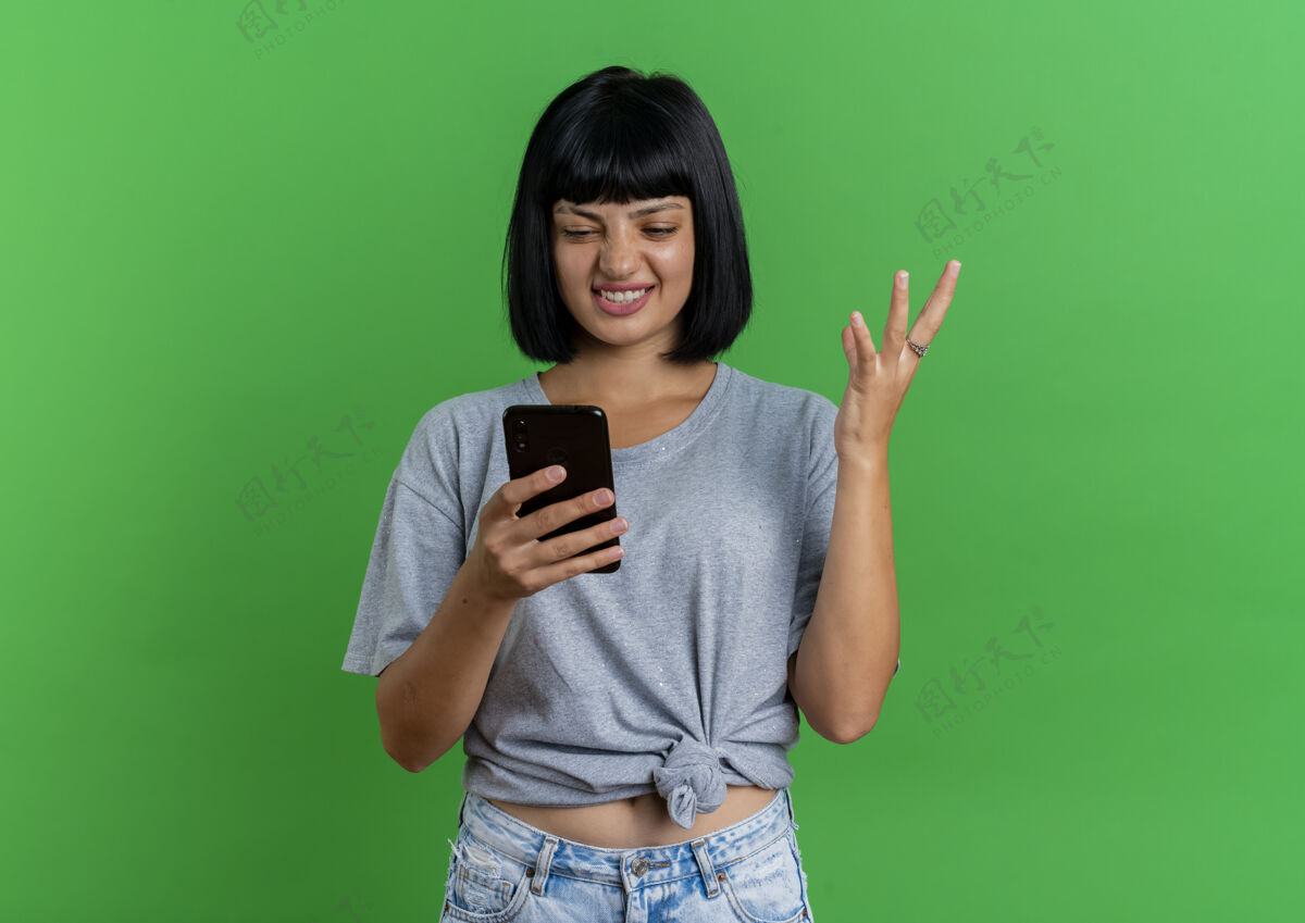 手恼怒的年轻黑发白种女孩举手 看着绿色背景上的手机和复印空间空间烦恼复制