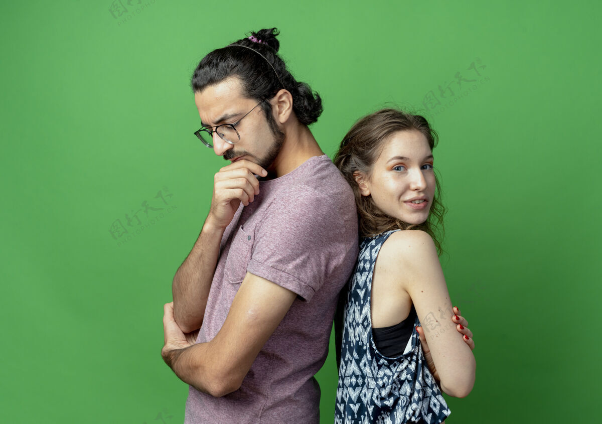 沉思一对年轻的夫妇 男人带着沉思的表情 女人微笑着背靠背地站在绿色的背景上情侣年轻表情