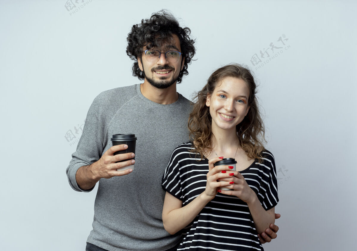 站着一对快乐的年轻夫妇站在白色的背景下 一边拿着手机 一边开心地看着摄像机脸情侣移动