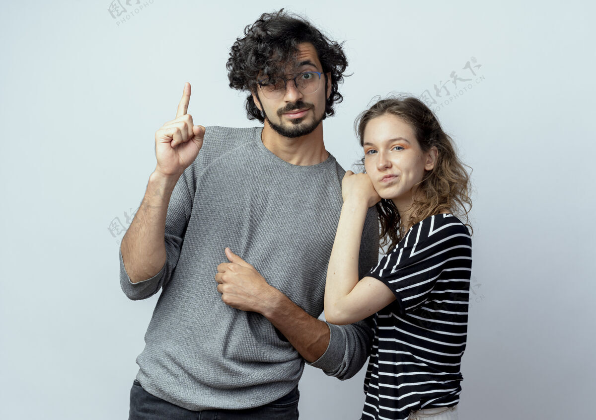 夫妻一对年轻的夫妇 男人和女人并排站在一起 男人伸出食指 而他的女朋友皱着眉头站在白色的背景上而皱眉年轻