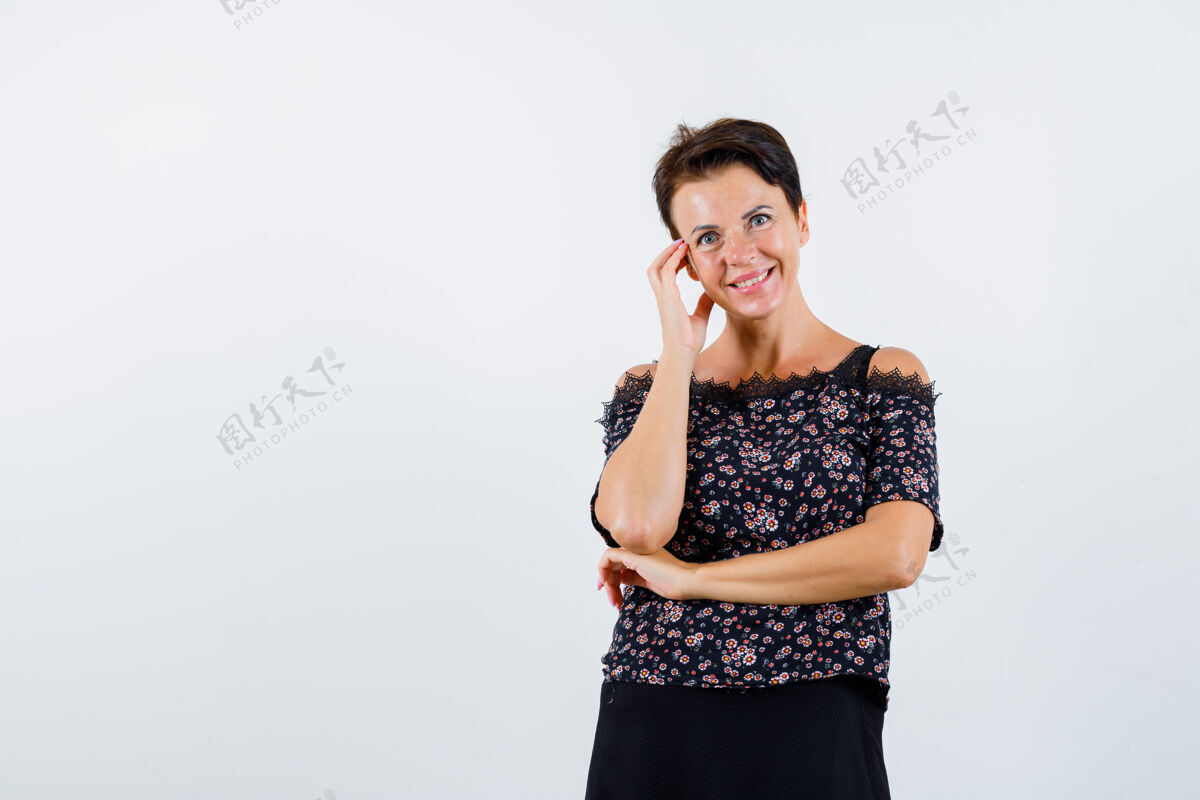脸颊一个穿着花衬衫的成熟女人 黑色的裙子 脸颊靠在手掌上 手挽在手肘下 看起来很迷人 前视图成熟微笑老年人
