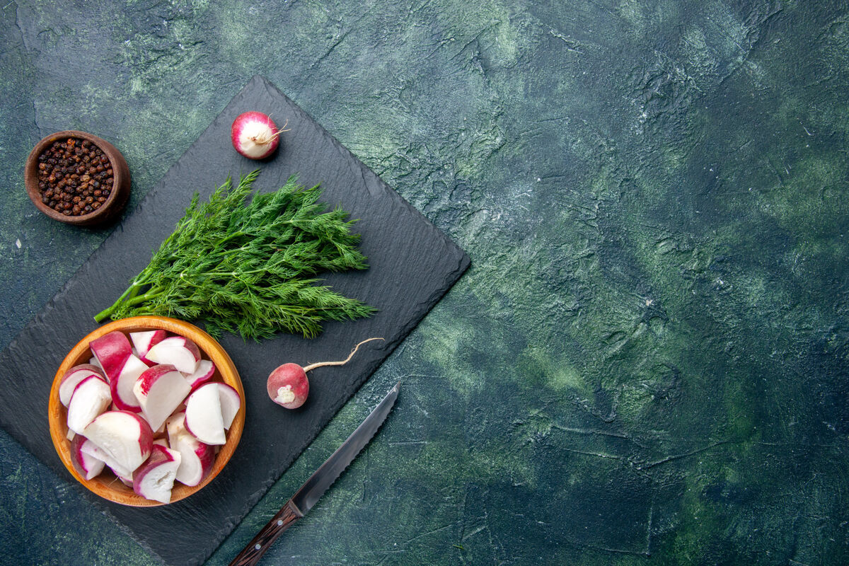 切割新鲜莳萝包和整个切碎萝卜刀的顶视图在黑色砧板的右侧 胡椒刀在绿-黑混合色背景上 有自由空间胡椒混合球