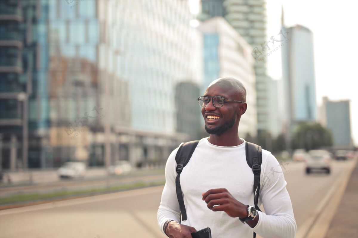 模特开朗微笑的非洲男性 戴着眼镜 穿着白色t恤 背着背包出门年轻城市背包