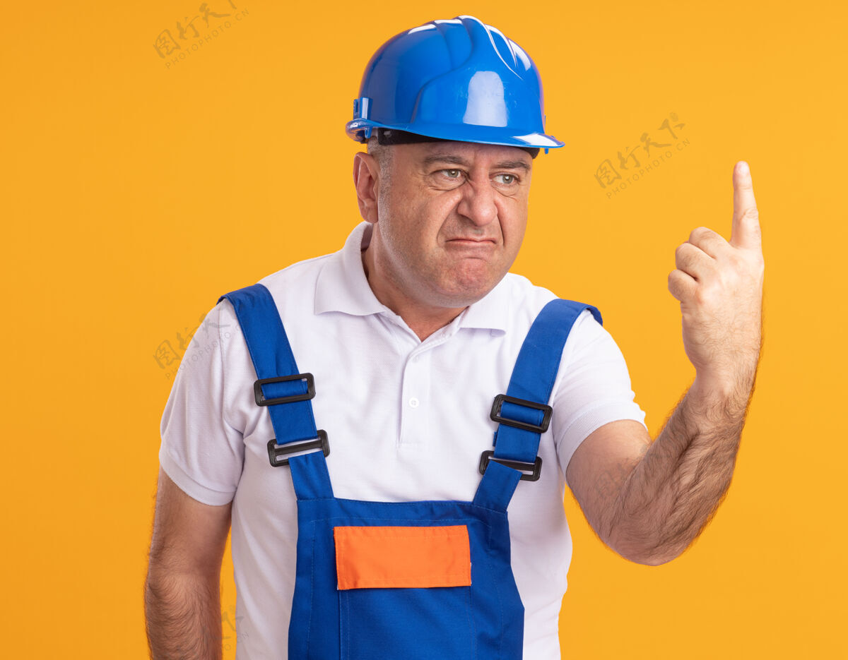 人恼怒的穿制服的成年建筑工人把食指孤立在橙色的墙上成人制服立场