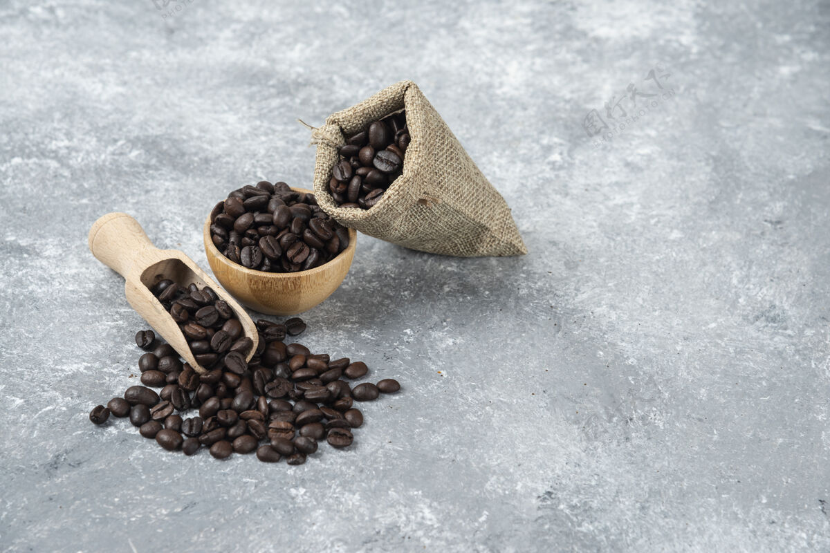 麻布装满烤咖啡豆的麻布和大理石表面的木碗黑种子庄稼