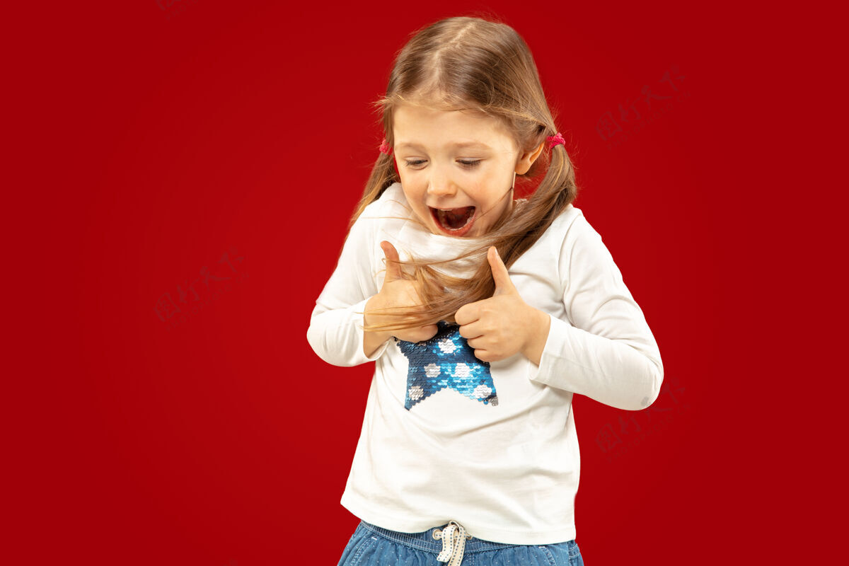 年轻美丽动情的小女孩被隔离在红色的背景上半长的快乐的孩子的肖像 显示一个手势 并指向上面部表情的概念 人类的情感 童年女孩积极乐趣