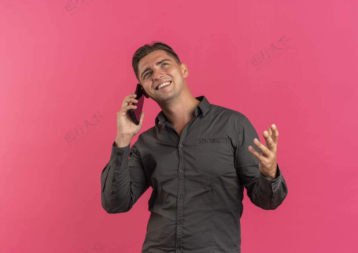 电话年轻微笑的金发帅哥在电话里说话 在粉色背景上看着孤立的复制空间英俊年轻金发