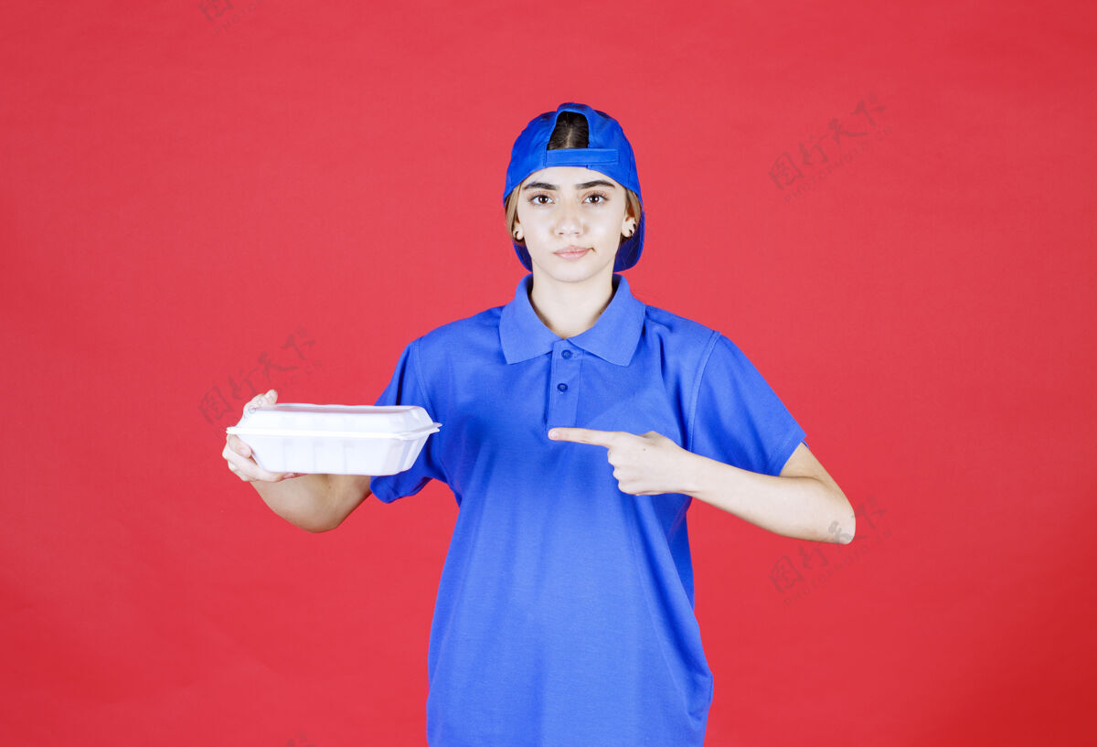 工人穿着蓝色制服的女快递员手里拿着一个白色的外卖箱送货呆在家里年轻人