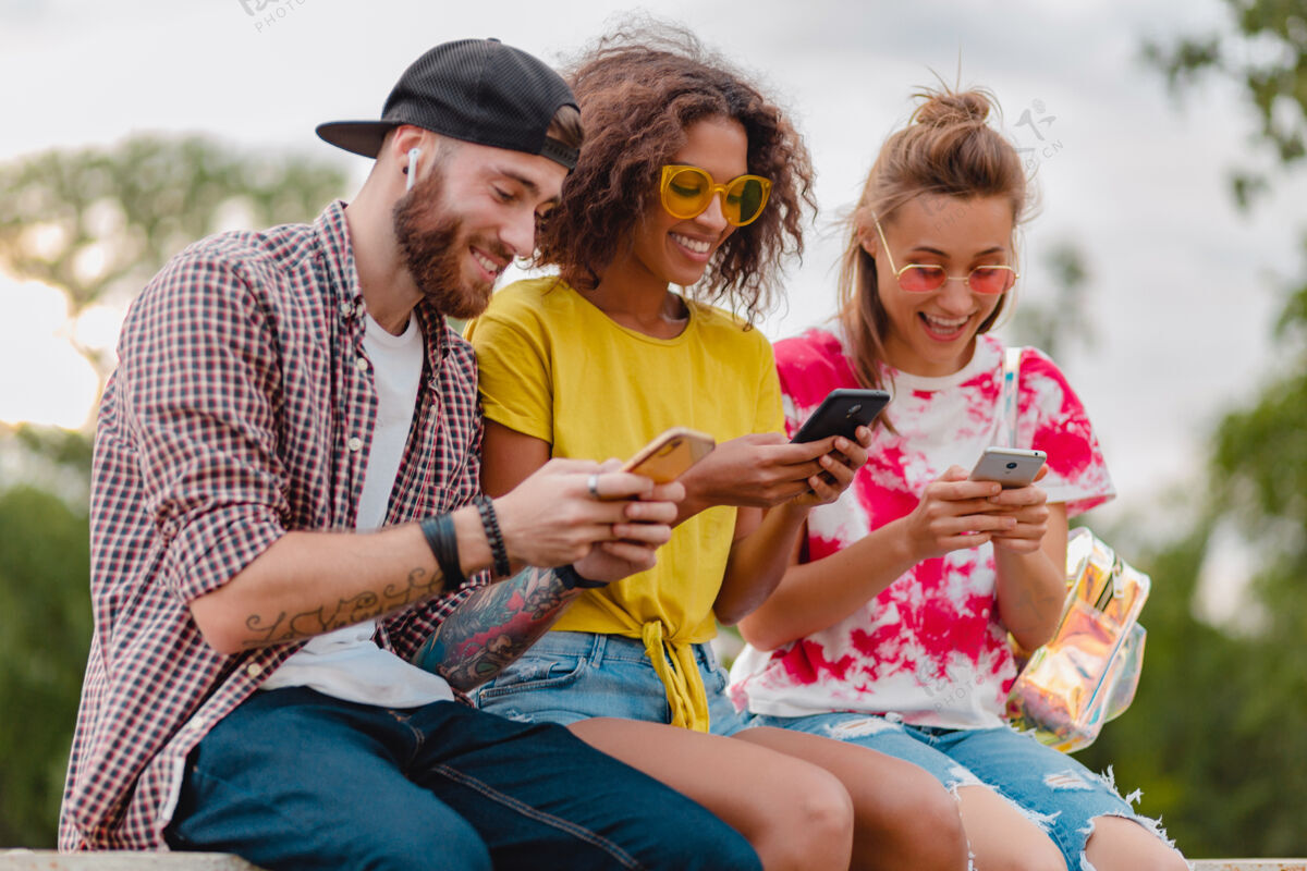 聪明快乐的年轻朋友坐在公园里用智能手机微笑公司女人积极无线