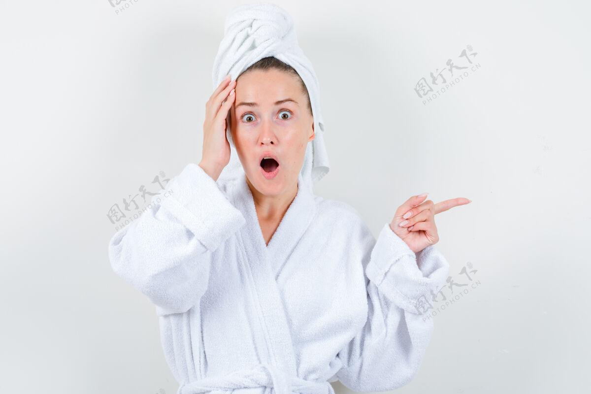 持有年轻的女士手举在头上 同时指着右边的白色浴衣 毛巾和期待惊讶 前视图成人头发自然
