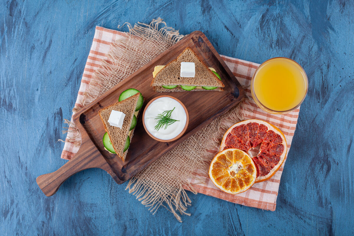 美味干菜旁边放一杯果汁 三明治 在木板上放上粗麻布餐巾 放上蓝色的美味叶果汁