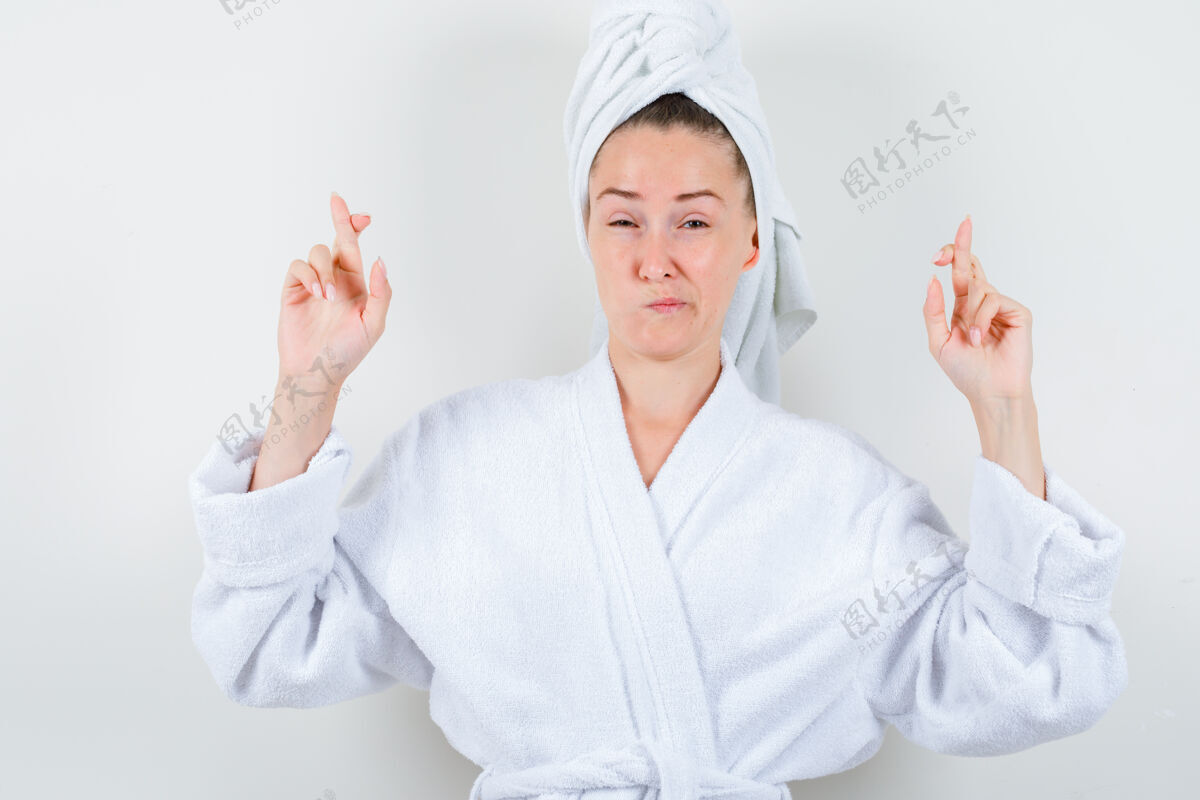 亚洲人年轻的女士在白色浴衣 毛巾和手指交叉看起来不满意 前视图微笑前面完美