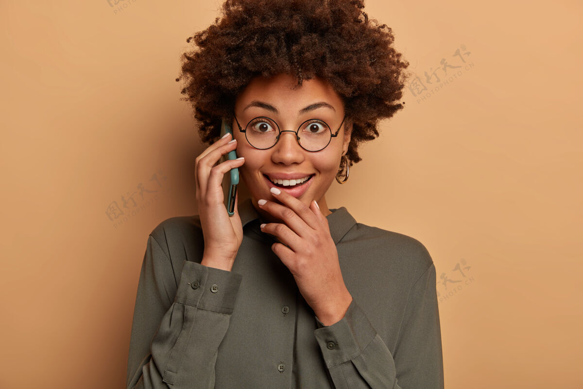 咯咯笑满意惊讶的美国黑人妇女在智能手机上愉快地交谈 对可怕的新闻有愉快的反应 讨论意想不到的谣言 享受愉快的交谈非洲女性衬衫