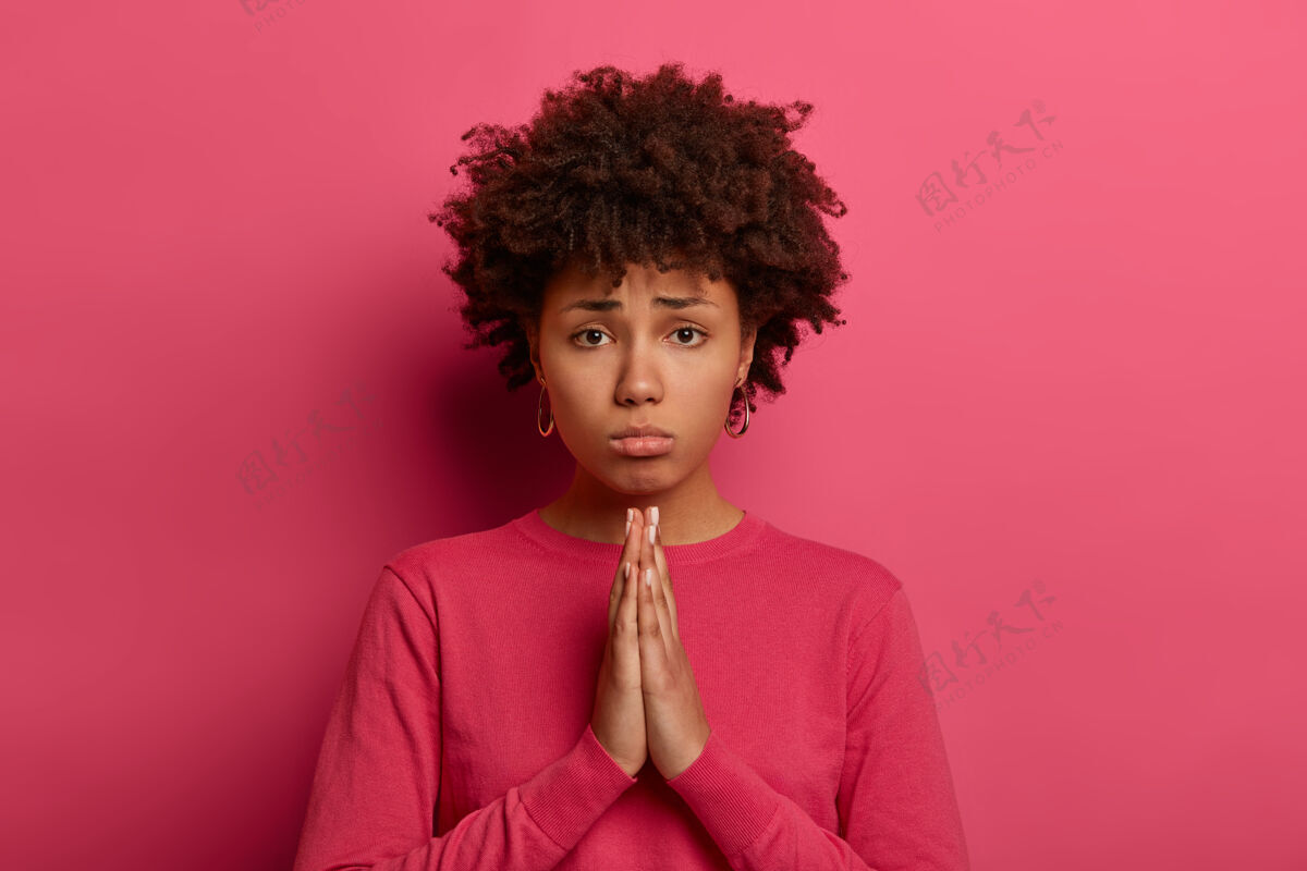 女性一个非洲发型的可怜女人双手合十 乞求帮助 有着天真胆小的悲伤表情 穿着粉色毛衣不满赞扬请