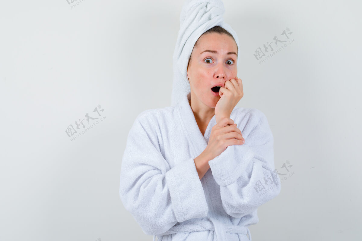 时尚年轻的女士手持拳头靠近嘴巴 穿着白色浴衣 脸上挂着毛巾 神情惊讶 眼前一亮干净近魅力