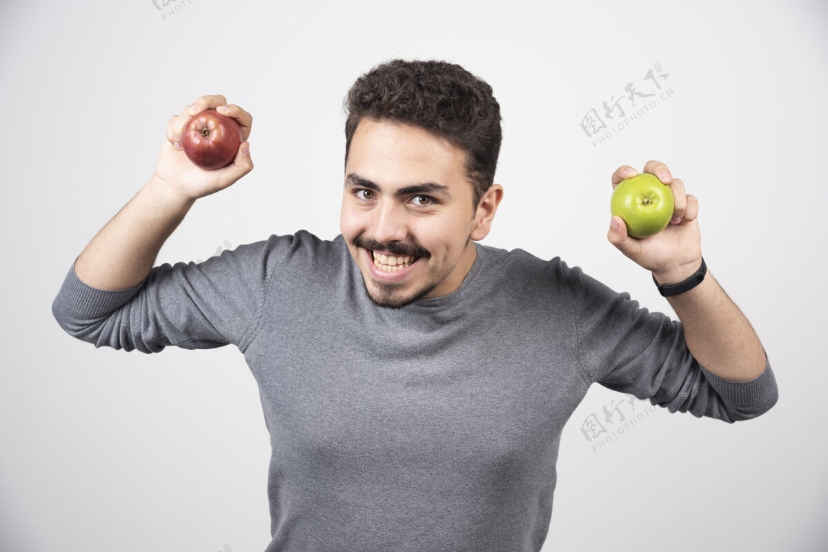 肖像黑发男人高高兴兴地拿着青苹果和红苹果水果欢呼模型