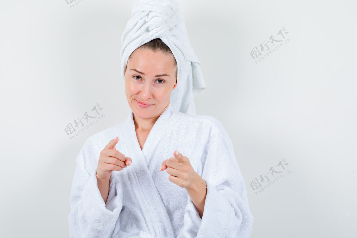 肖像穿着白色浴袍的年轻女子 用毛巾指着镜头 看上去很懂事 正对着镜头人人时尚