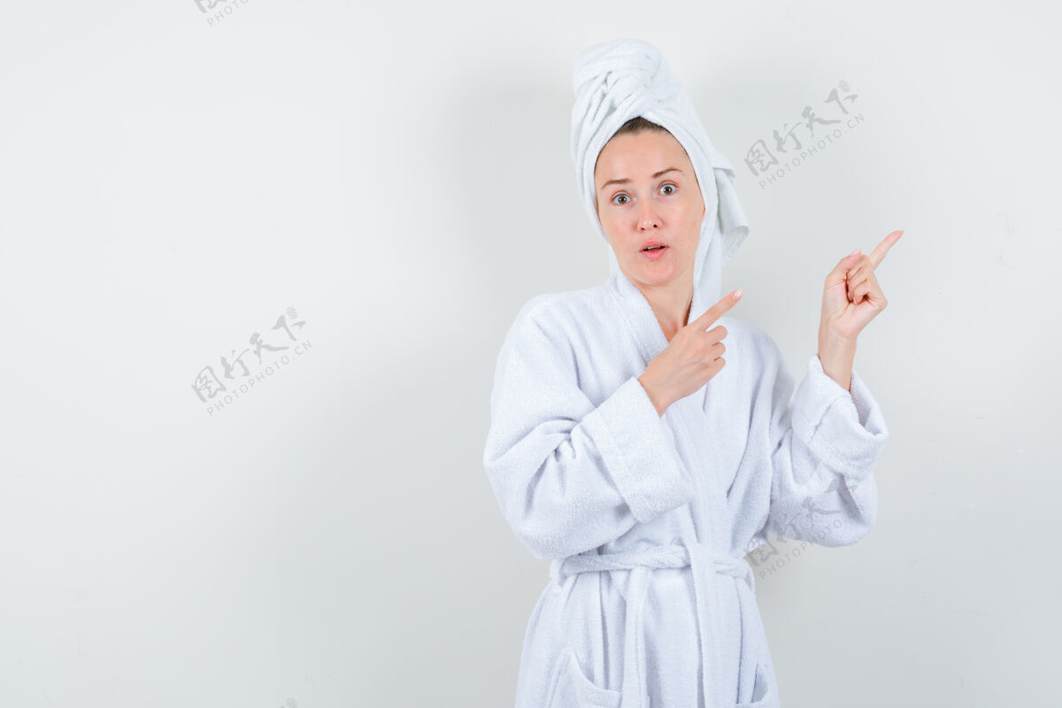 女孩画像中的年轻女子指着右上角的白色浴衣 毛巾和看困惑的前视图乐趣时尚浴袍