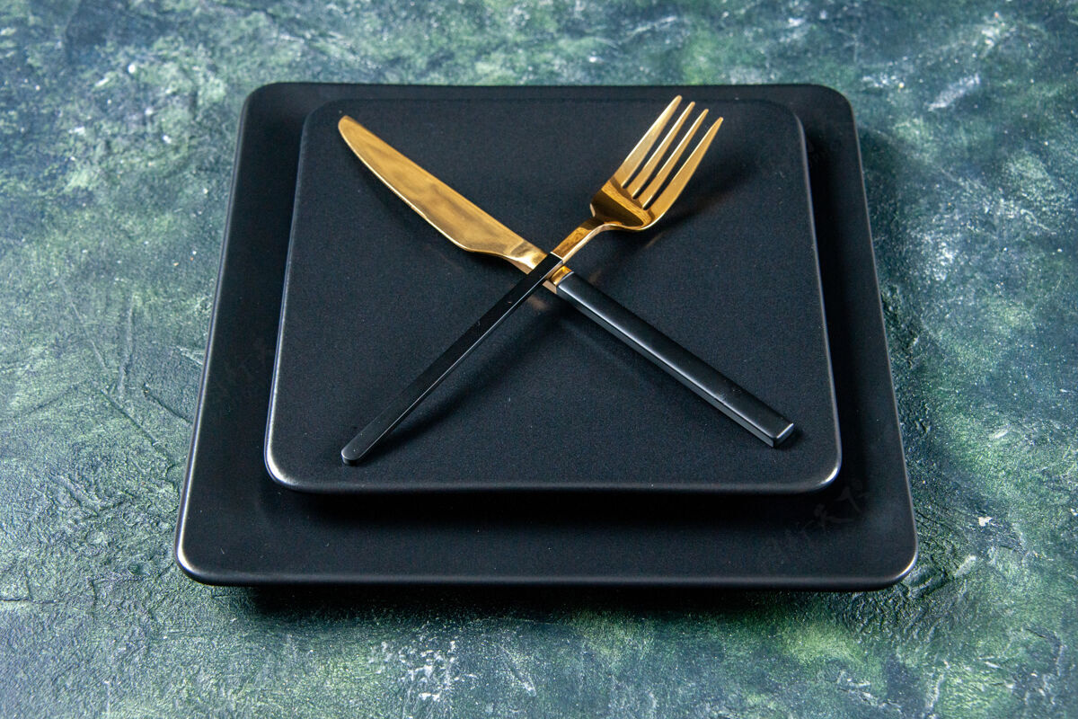 厨房正面图黑色的盘子和金色的刀叉交叉在黑暗的背景上金色晚餐深色
